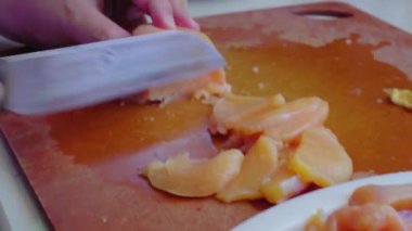 Kadının elleri bıçakla ince bir tavuk filetosunu kesiyor. Masada tavuk eti.