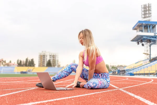 Athletic girl playing sports stretching and yoga on the mat for watching fitness videos online on a laptop at home. Female doing yoga on the internet with a laptop PC. Conducts online training