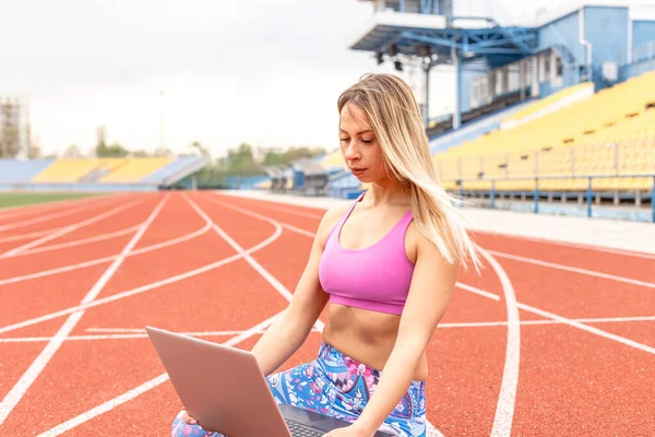 Athletic girl playing sports stretching and yoga on the mat for watching fitness videos online on a laptop at home. Female doing yoga on the internet with a laptop PC. Conducts online training