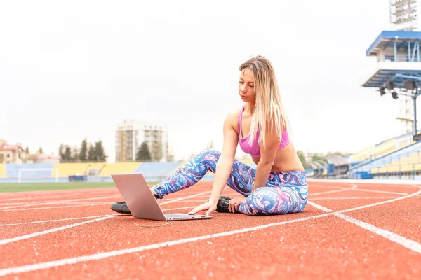 Athletic girl playing sports stretching and yoga on the mat for watching fitness videos online on a laptop at home. Female doing yoga on the internet with a laptop PC. Conducts online training