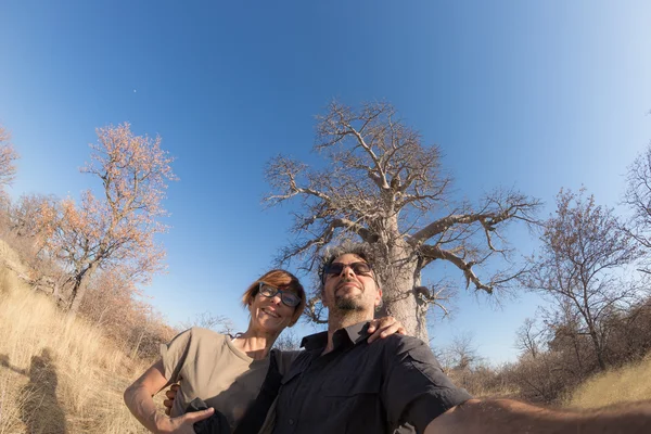 Casal tirando selfie perto da planta Baobab na savana africana com céu azul claro. Fisheye vista de baixo. Safári selvagem e aventura na África . — Fotografia de Stock