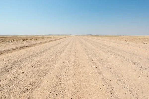 Camino recto de grava que cruza el colorido desierto de Namib, en el majestuoso Parque Nacional Namib Naukluft, el mejor destino de viaje en Namibia, África . — Foto de Stock