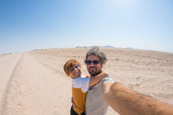 Adult couple taking selfie on gravel road in the Namib desert, Namib Naukluft National Park, main travel destination in Namibia, Africa. Fisheye view in backlight, adventure in Africa. — Stock Photo, Image
