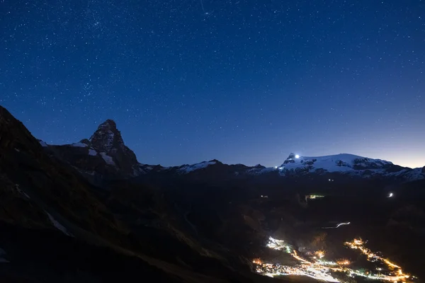 Aosta Vadisi, İtalya için gece, ünlü kayak merkezi içinde parlayan Breuil Cervinia köyünün havadan görünümü. Matterhorn (Cervino) dağ tepe ve Monte Rosa buzullar üzerinde harika yıldızlı gökyüzü. — Stok fotoğraf