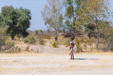 Caprivi, Namibia - August 20, 2016: Poor woman walking on the roadside in the rural Caprivi Strip, the most populated region in Namibia, Africa. clipart