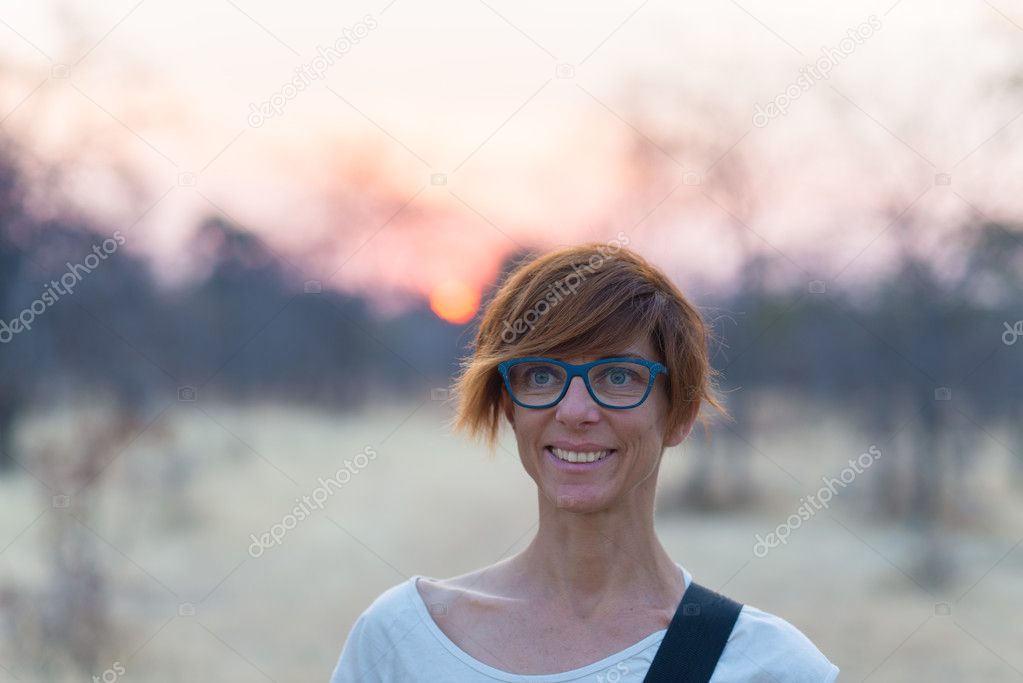 Portrait of a red haired woman with green eyes, eyeglasses and smiling facial expression. Sunset at the horizon. Shot outdoors with natural background, cold toned.