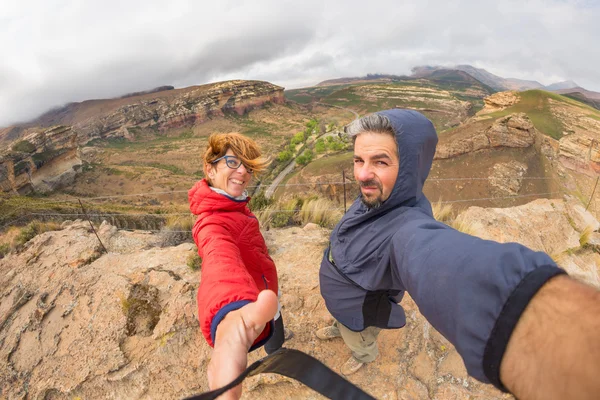 Casal com braços estendidos tirando selfie no cume da montanha ventosa no majestoso Golden Gate Highlands National Park, África do Sul. Conceito de aventura e pessoas itinerantes. Visão de olho de peixe . — Fotografia de Stock