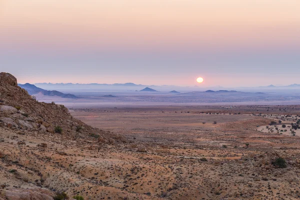 Colorido atardecer sobre el desierto de Namib, Aus, Namibia, África. Naranja rojo violeta claro cielo en el horizonte, rocas brillantes y cañón en primer plano . — Foto de Stock