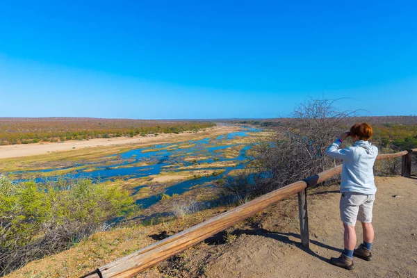 Turista olhando para o panorama com binocular do ponto de vista sobre o rio Olifants, paisagem cênica e colorida com vida selvagem no Parque Nacional Kruger, famoso destino de viagem na África do Sul . — Fotografia de Stock