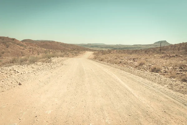 Kavics kanyargós út keresztezi a Namíb-sivatag, a fenséges Namíb Naukluft nemzeti parkban, Namíbia, Afrika legjobb úticél. Tónusú kép, vintage régi retro szűrő. — Stock Fotó