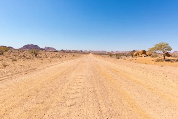 Gravel 4x4 road crossing the colorful desert at Twyfelfontein, in the majestic Damaraland Brandberg, scenic travel destination in Namibia, Africa. — Stock Photo, Image