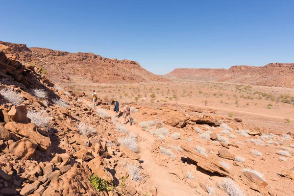 Twyfelfontein, Namíbia - 27 de agosto de 2016: Grupo de turistas caminhando no deserto em Twyfelfontein, local de gravuras de rocha herança mundial em Damaraland, Namíbia. Conceito de aventura e exploração em — Fotografia de Stock