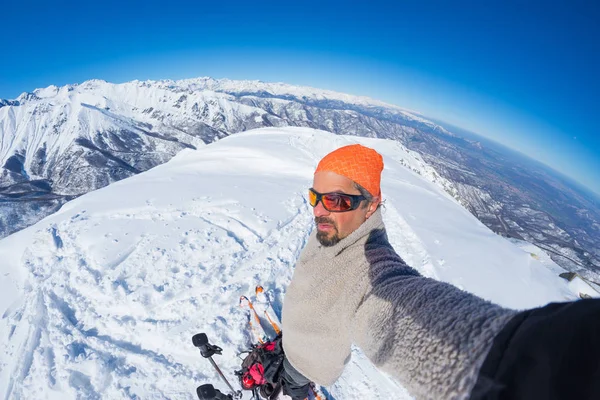 Erwachsener alpiner Skifahrer mit Bart, Sonnenbrille und Hut, der ein Selfie auf einer schneebedeckten Piste in den wunderschönen italienischen Alpen mit klarem blauen Himmel macht. Konzept von Fernweh und Abenteuer am Berg. Weitwinkelspalte — Stockfoto