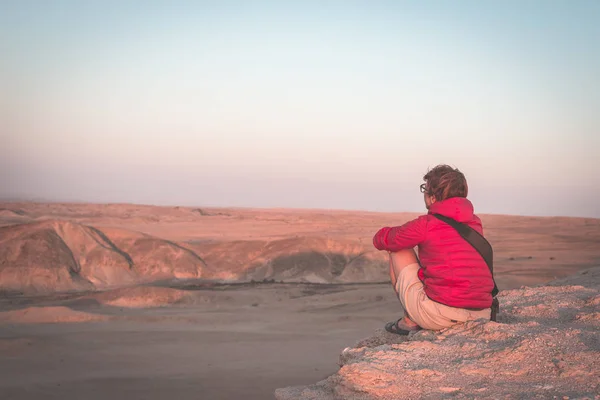 Visão traseira da mulher sentada em rochas e olhando para a vista expansiva sobre o deserto cênico do Namib ao entardecer. Viajar no Parque Nacional Namib Naukluft, Namíbia, África . — Fotografia de Stock