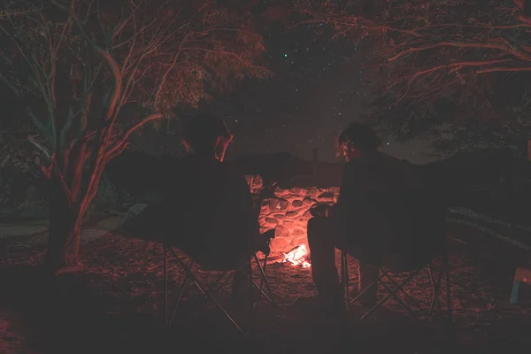 Un paio seduti a bruciare il fuoco del campo di notte. Campeggio nella foresta sotto il cielo stellato, Namibia, Africa. Avventure estive ed esplorazioni nei Parchi Nazionali Africani. Concentrazione selettiva sul fuoco. Tonnellata — Foto Stock