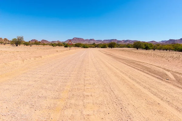 Gravel 4x4 road crossing the colorful desert at Twyfelfontein, in the majestic Damaraland Brandberg, scenic travel destination in Namibia, Africa. — Stock Photo, Image