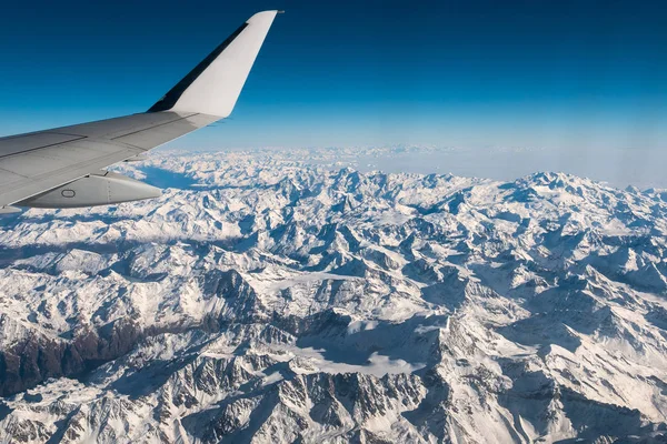 Vista aérea de los Alpes suizos italianos en invierno, con ala de avión genérica. Cordillera nevada y glaciares. Vista expansiva, cielo azul claro . —  Fotos de Stock