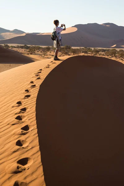 Tourist holding smart phone and taking photo at scenic sand dunes at Sossusvlei, Namib desert, Namib Naukluft National Park, Namibia. Adventure and exploration in Africa. — Stock Photo, Image