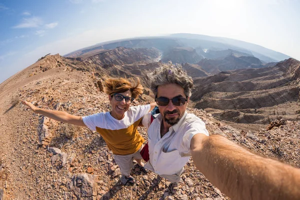 Casal levando selfie no Fish River Canyon, destino de viagem cênica no sul da Namíbia. Fisheye vista de cima na luz de fundo . — Fotografia de Stock