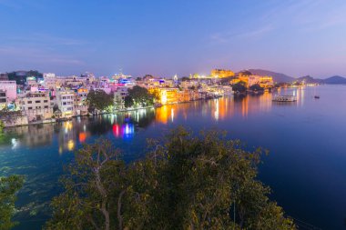 Geceleri Udaipur 'da parlak bir şehir manzarası. Lake Pichola üzerinde ışıklar yansıtan görkemli şehir Sarayı, Rajasthan, Hindistan seyahat hedef