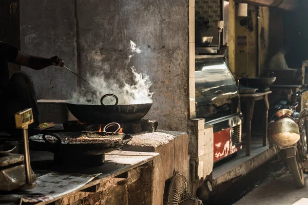 Hombre irreconocible cocinando en una gran sartén o wok en un pequeño puesto de comida callejera. El humo blanco que sale de la sartén, mano y brazo solo es visible. Comida callejera en India . —  Fotos de Stock