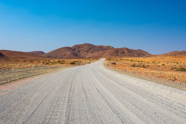 Gravel 4x4 road crossing the colorful desert at Twyfelfontein, in the majestic Damaraland Brandberg, scenic travel destination in Namibia, Africa. — Stock Photo, Image