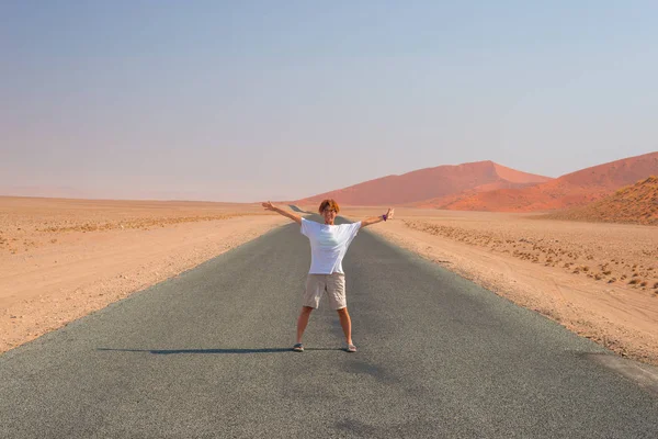 Kvinna med utsträckta armar står på grusvägen som passerar den Namiböknen, i Namib Naukluft National Park, huvudsakliga resmål i Namibia, Afrika. — Stockfoto