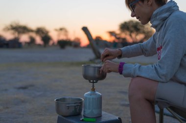 Gaz kamp sitedeki gece karanlığında sobası ile yemek kadın. Gaz yakıcı, pot ve kaynar su gelen duman. Afrika Milli Parklar Maceraları.