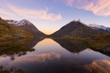 Gün batımında parlayan görkemli kayalık dağ doruklarına yansıması ile pastoral topraklarda yüksek irtifa dağ gölü. Alpler üzerinde geniş açılı görünüş.