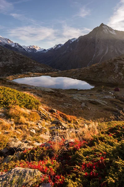Camping med tält nära hög höjd lake på Alperna. Reflektion av snötäckta bergskedjan och natursköna färgglada himmel i solnedgången. Äventyr och utforskning. — Stockfoto