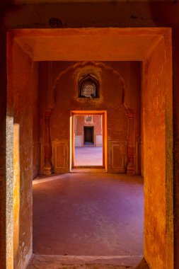 Lined doors and passages in orange toned corridor with decorated walls. Interior of the majestic Amber Fort, Jaipur, travel destination in Rajasthan, India. clipart