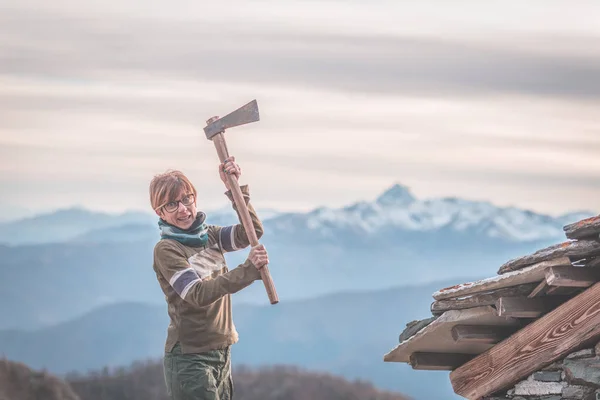 Mujer enojada sosteniendo un hacha. Fondo escénico con picos de montaña, valle brumoso y cielo malhumorado, en los Alpes . — Foto de Stock