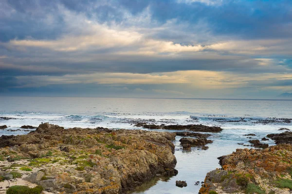 Línea costera rocosa en el océano en De Kelders, Sudáfrica, famosa por la observación de ballenas. Temporada de invierno, cielo nublado y dramático . — Foto de Stock