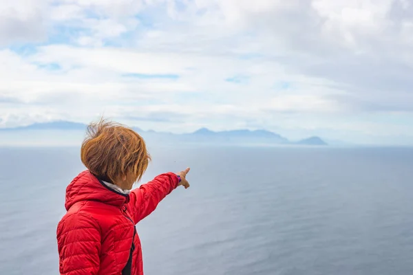 Turista apontando com o dedo a linha costeira rochosa em Cape Point, Table Mountain National Park, África do Sul. Estação de inverno, céu nublado e dramático . — Fotografia de Stock