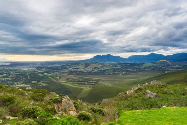 Cape Town, Güney Afrika çevresinde yeşil dağların üzerinden uçan Yamaçparaşütü. Kış sezonu, bulutlu ve dramatik gökyüzü. Tanınmayan insanlar.
