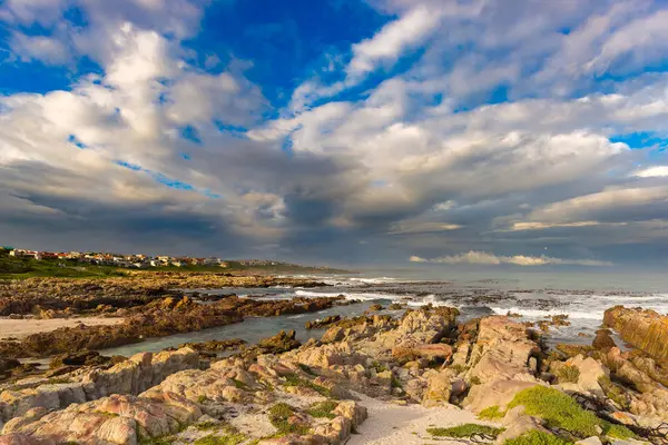 Klippiga kustlinje på havet på De Kelders, Sydafrika, känd för valskådning. Vintersäsongen, molnigt och dramatisk himmel. — Stockfoto