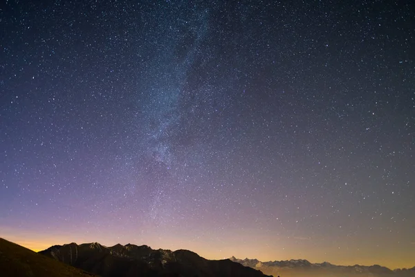 De prachtige sterrenhemel op Kerstmis en de majestueuze hoge bergketen van de Italiaanse Franse Alpen, met gloeiende dorpen hieronder en maanlicht. — Stockfoto