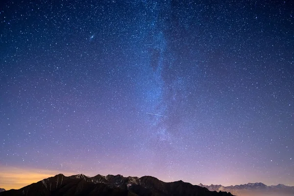 Le ciel étoilé merveilleux pendant la période de Noël et la majestueuse chaîne de haute montagne des Alpes françaises italiennes, avec des villages lumineux en dessous et clair de lune . — Photo