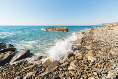 Çakıl, taş ve kayalar, boş bir plaj Liguria, Kuzey İtalya sert kayalık Sahili kırma su dalgaları. Açık mavi gökyüzü, geniş açılı görünüş.