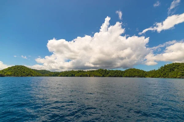 Costa rocosa de la isla manchada por islotes y cubierta por una densa selva verde en el colorido mar de las remotas islas Togean (o islas Togian), Sulawesi Central, Indonesia . —  Fotos de Stock