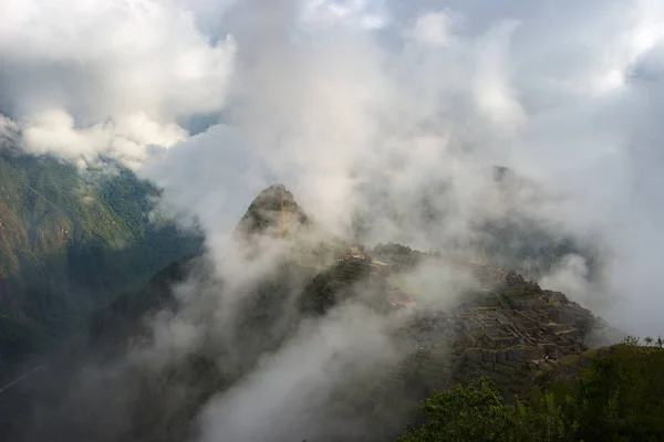 Machu Picchu iluminado pela primeira luz solar saindo das nuvens de abertura. A cidade do Inca é o destino de viagem mais visitado no Peru. Névoa, nuvens e nevoeiro que cobrem o vale . — Fotografia de Stock
