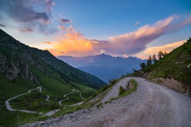 Dirt mountain road leading to high mountain pass in Italy (Colle delle Finestre). Expasive view at sunset, colorful dramatic sky, adventures in summer time, Italian Alps. clipart