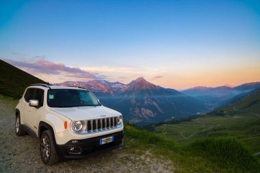 Beyaz Jeep Renegade yukarıdan İtalyan Alpleri panoramik noktasında toprak yol üzerinde park etmiş. Gün batımında, Kurtlar Vadisi buğu renkli gökyüzü.