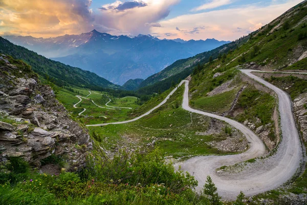 Unbefestigte Bergstraße, die zum Hochpass in Italien führt (colle delle finestre). Expasive Aussicht bei Sonnenuntergang, farbenfroher dramatischer Himmel, Abenteuer im Sommer, italienische Alpen. — Stockfoto