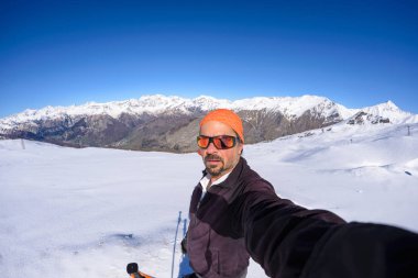 Açık mavi gökyüzü ile güzel İtalyan Alpleri'nde karlı yamaç selfie alarak yetişkin alpin kayakçı sakal, güneş gözlüğü ve şapka, ile. Yolculuk tutkusu ve maceralar dağ kavramı. Geniş açı fishe
