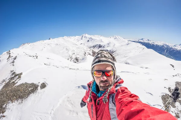Adult alpin skier with beard, sunglasses and hat, taking selfie on snowy slope in the beautiful italian Alps with clear blue sky. Concept of wanderlust and adventures on the mountain. Wide angle fishe — Stock Photo, Image