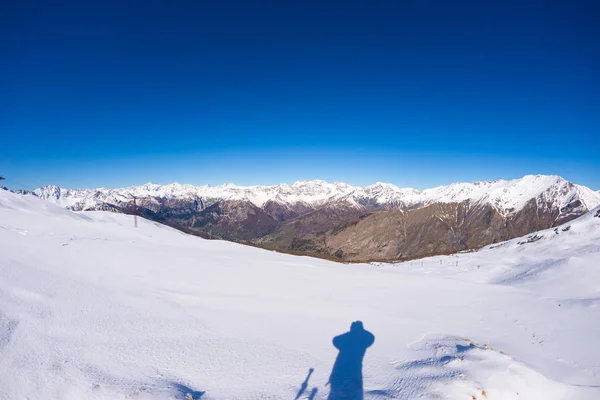 Vista ad ampio angolo di una stazione sciistica in lontananza con eleganti cime montane derivanti dall'arco alpino durante la stagione invernale. Provincia di Torino confine Italia Francia . — Foto Stock