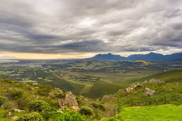 Parapente survolant les montagnes verdoyantes autour de Cape Town, Afrique du Sud. Saison d'hiver, ciel nuageux et dramatique. Des gens méconnaissables . — Photo