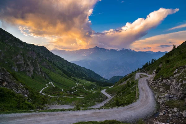 Strada sterrata di montagna che porta al colle delle Finestre. Vista panoramica al tramonto, cielo colorato e drammatico, avventure in estate, Alpi italiane . — Foto Stock