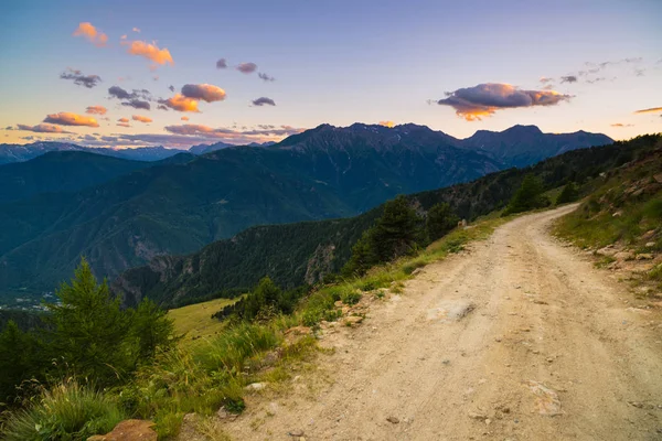 Dirt mountain road leading to high mountain pass in Italy. Expasive view at sunset, colorful dramatic sky, adventures in summer time, Italian Alps. — Stock Photo, Image
